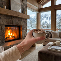 Thumbnail for Hand holding a hot chocolate by a fireplace, wearing the rose gold Crystal Bar Bracelet