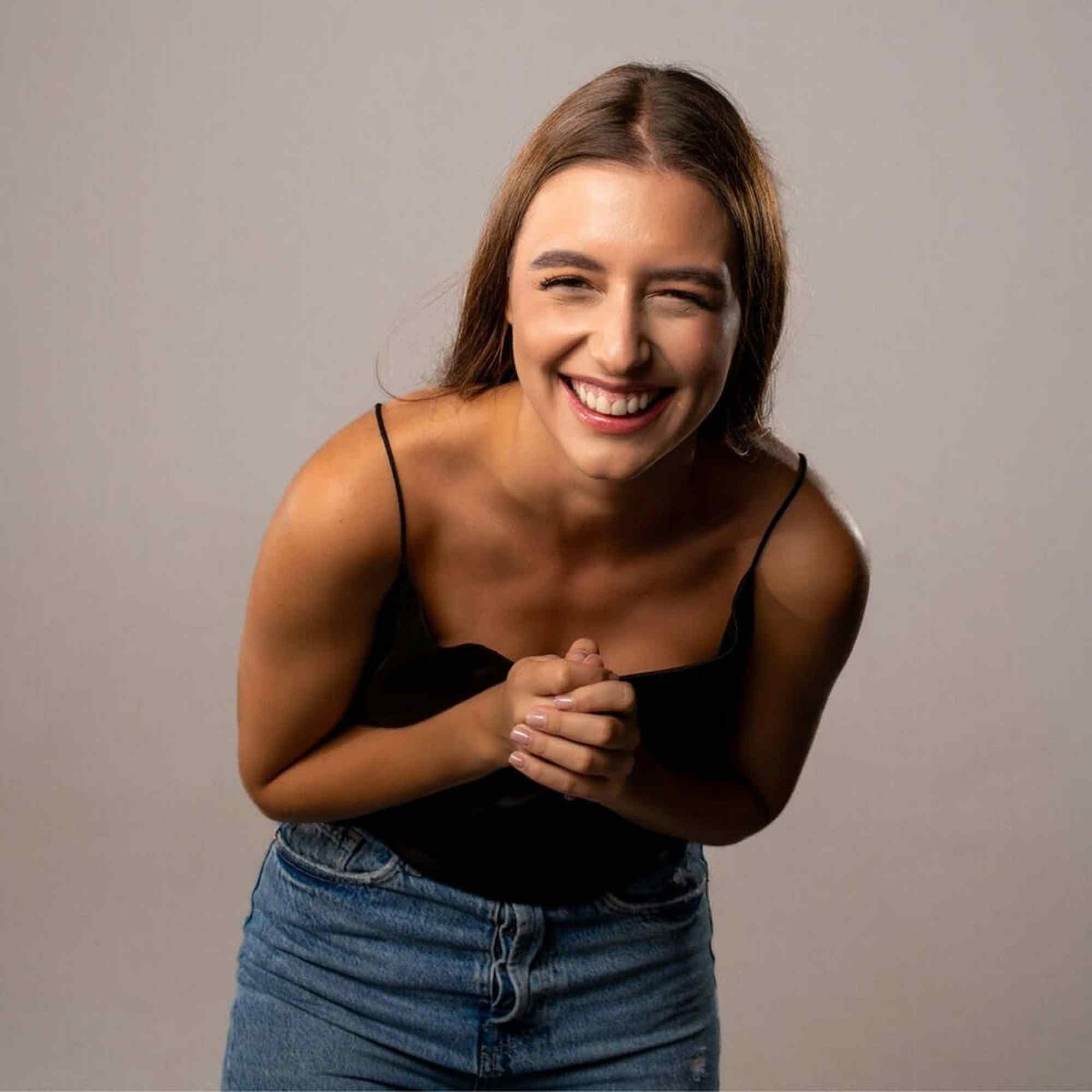 Smiling woman in casual outfit radiating joy and happiness against a neutral background.