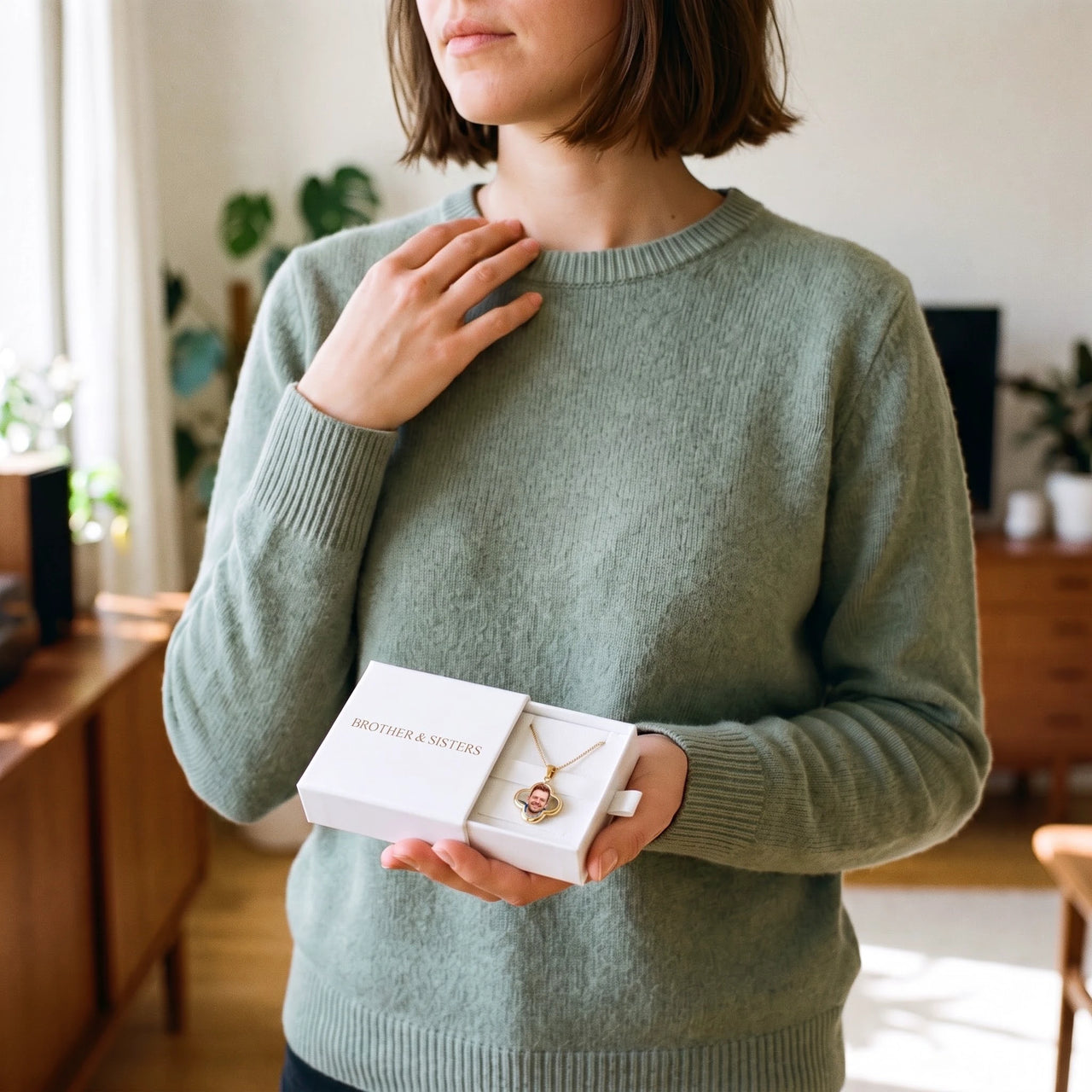 Woman in a green sweater holding the Brother & Sisters gift box with the gold clover photo necklace inside | SKU: TPH-CLVN-GOLD