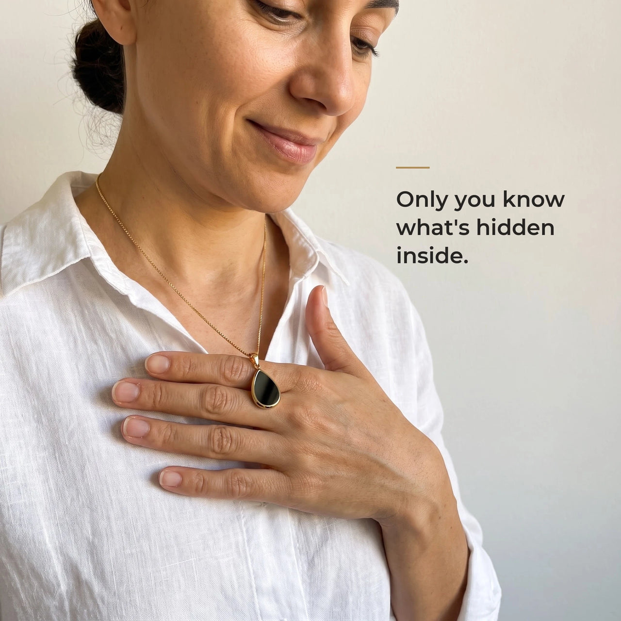 Woman holding the black teardrop pendant on its gold chain against her chest, only she knows the photo inside | SKU: TPH-DRPN-GOLD