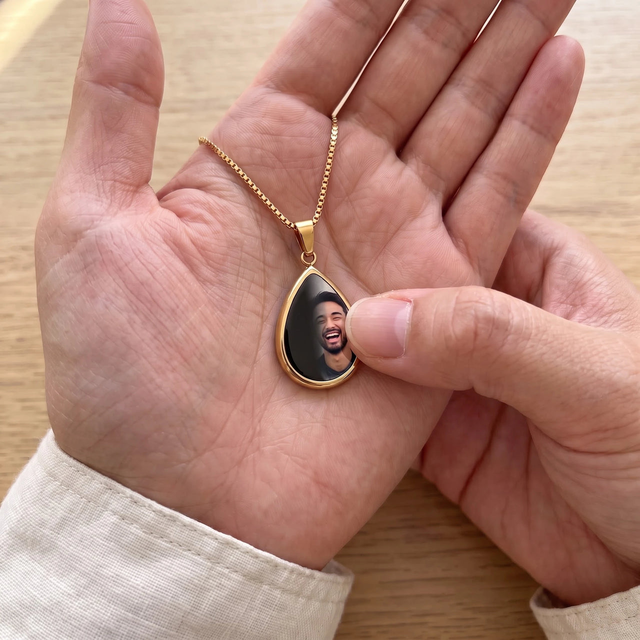 Thumb warming the gold teardrop pendant: the hidden photo appears under the thumb while the rest stays black | SKU: TPH-DRPN-GOLD