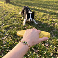Thumbnail for Customer photo: the gold heart bracelet with her border collie's photo, her dog in the background | SKU: TPH-HRTB-GOLD